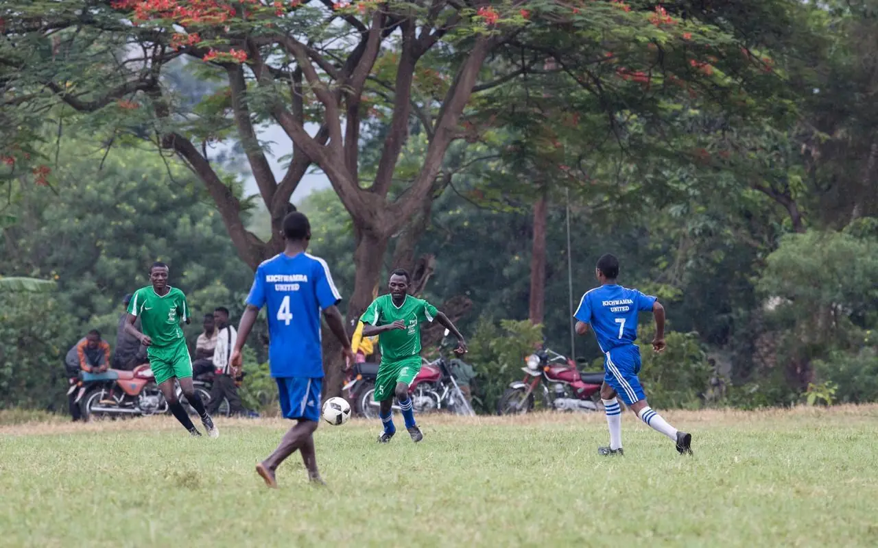 Youth soccer match in grassy field under large tree, Kyambura Gorge Lodge, Queen Elizabeth NP, Uganda