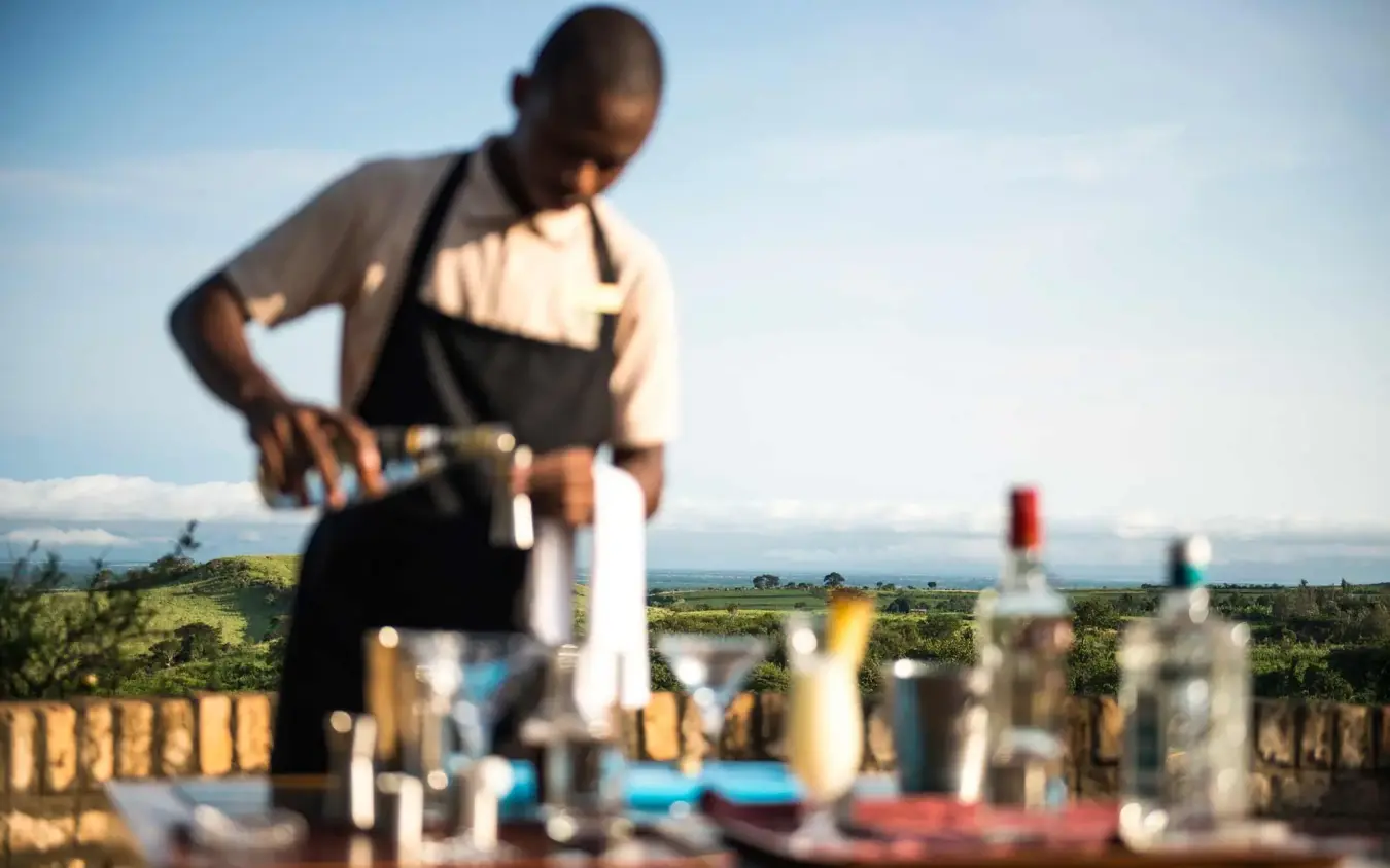 Staff member preparing drinks at outdoor bar setup, Kyambura Gorge Lodge, Queen Elizabeth NP, Uganda