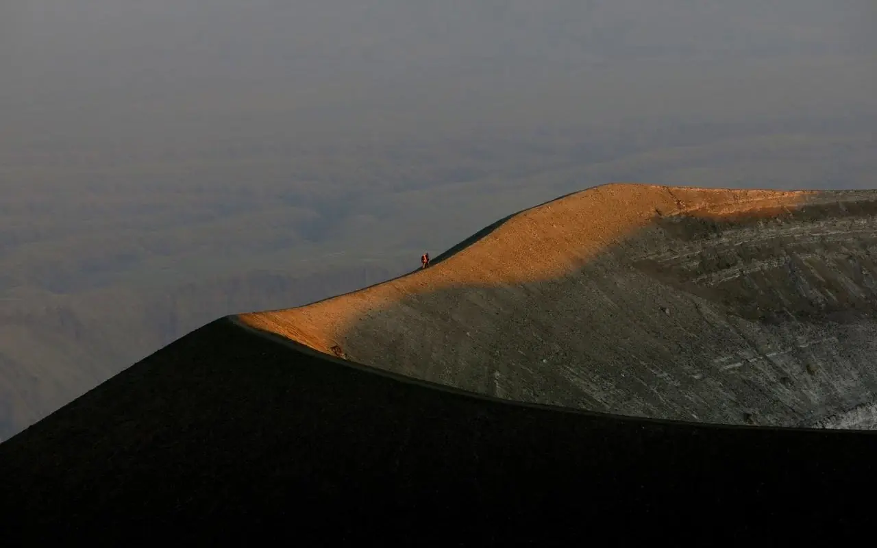Golden sunlit volcanic cone ridge against misty valley