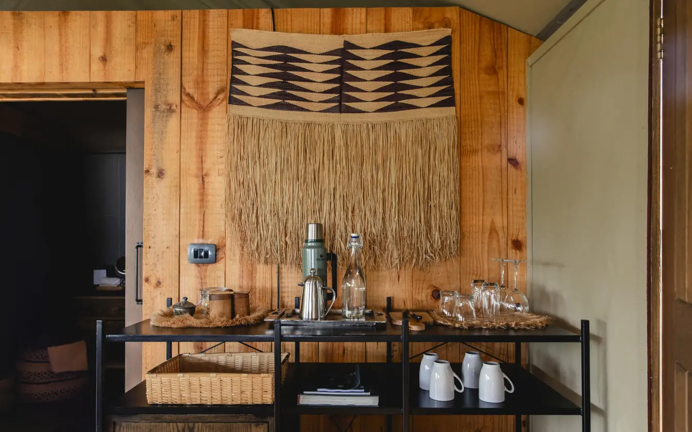 Wooden bar counter with woven wall hanging and glassware, Magashi Camp, Akagera National Park, Rwanda