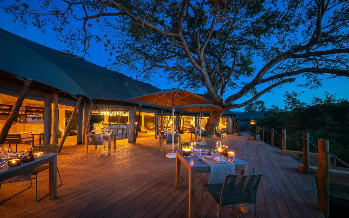 Wooden deck dining area under acacia tree at dusk, Magashi Camp, Akagera National Park, Rwanda