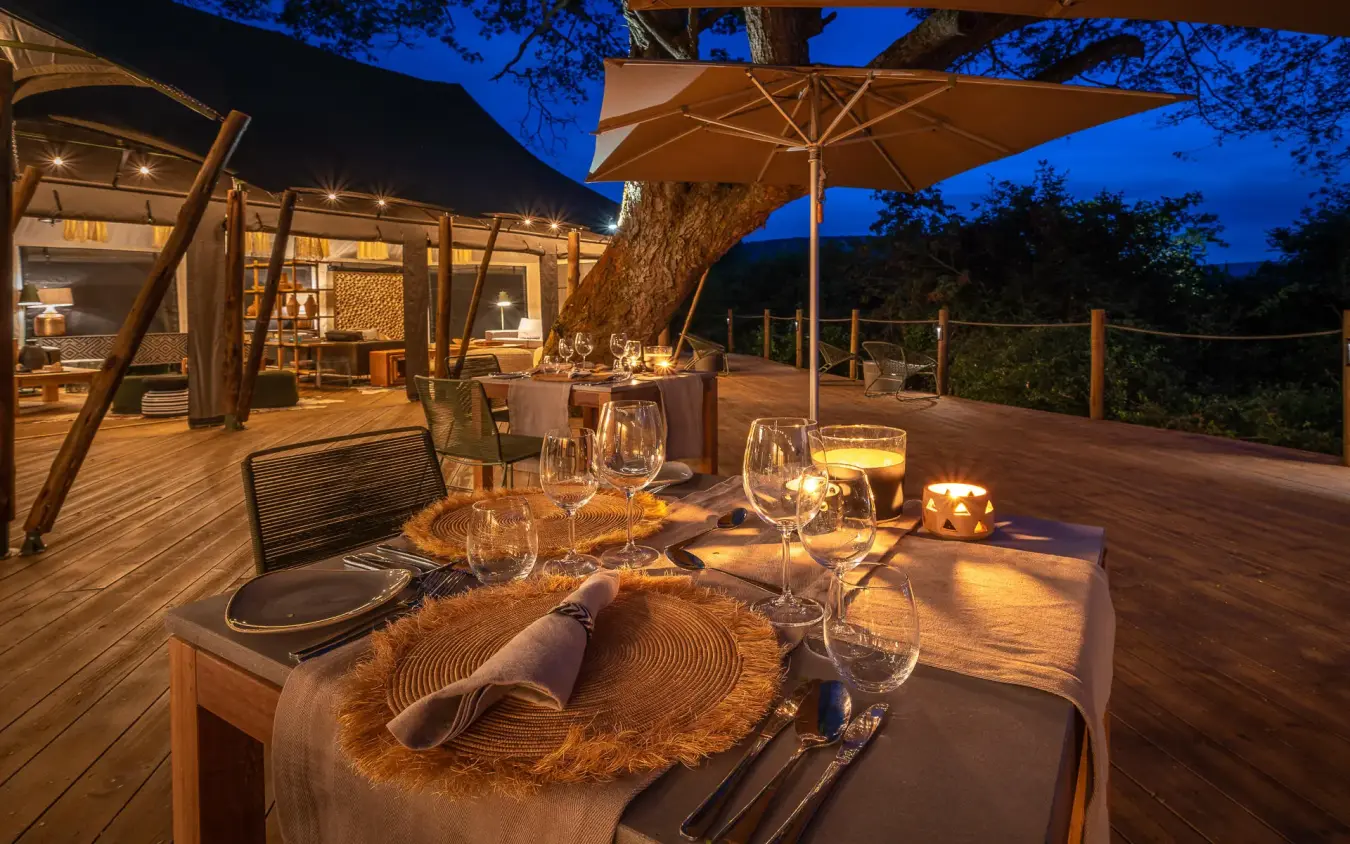 Outdoor dinner table set under umbrella at dusk, Magashi Camp, Akagera National Park, Rwanda