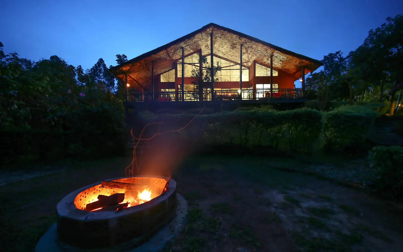 Illuminated lodge building at dusk with firepit in foreground, Mahogany Springs, Bwindi Impenetrable Forest, Uganda