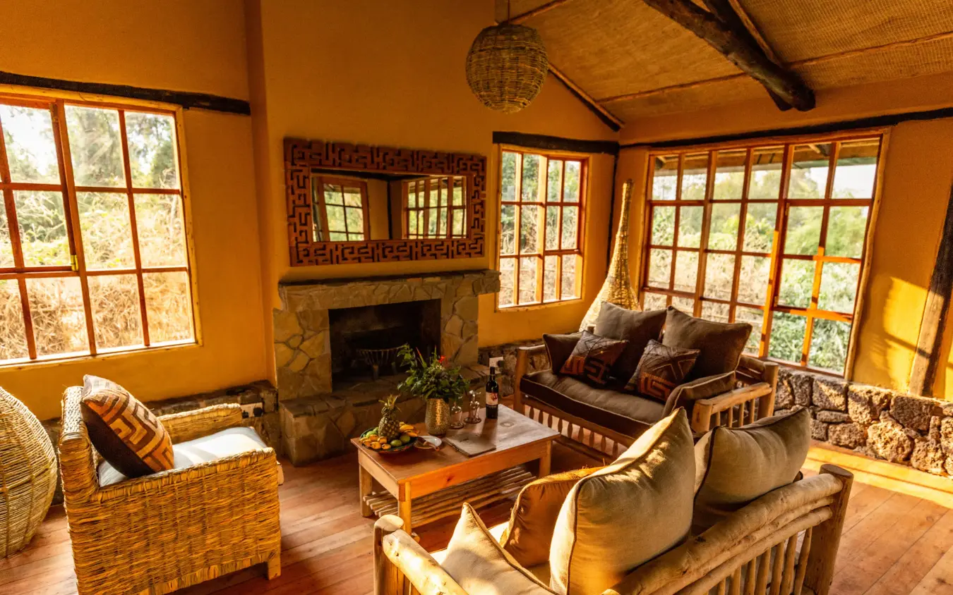 Warm orange lounge with fireplace and large windows overlooking forest, Mount Gahinga Lodge, Mgahinga National Park, Uganda