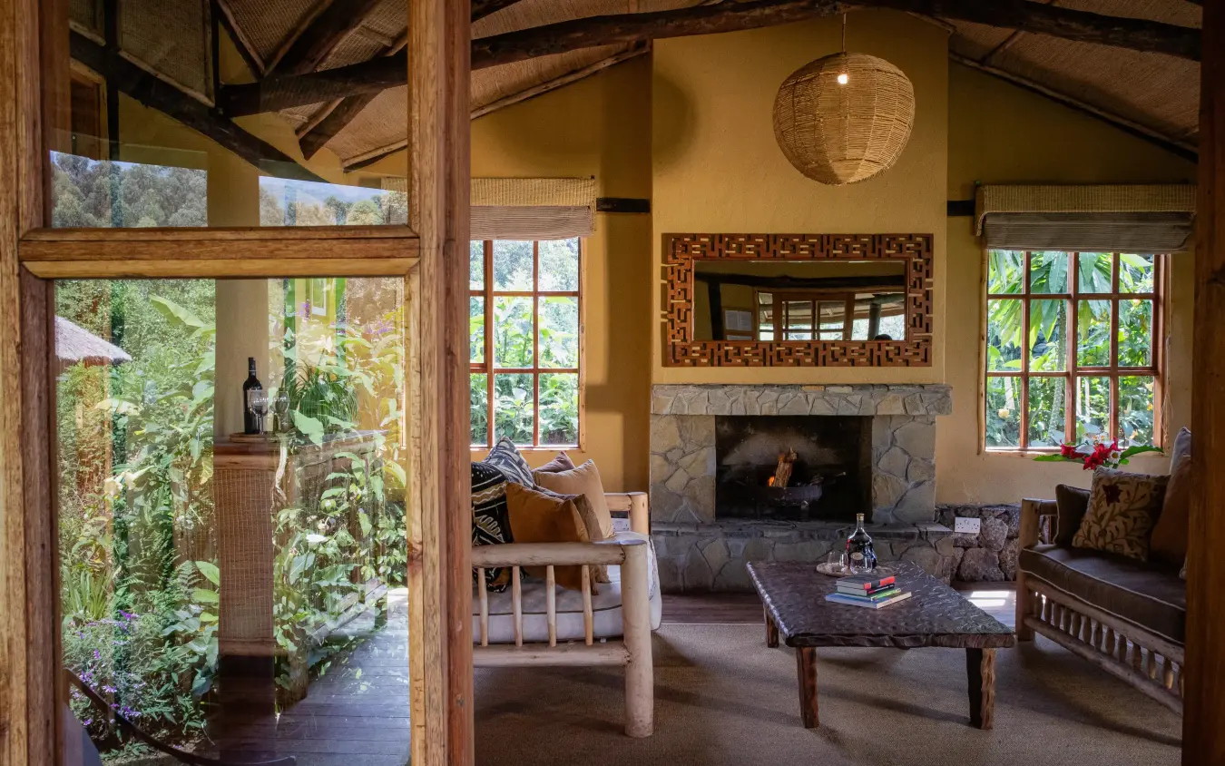 Interior lounge with fireplace, wooden beams, and garden views, Mount Gahinga Lodge, Mgahinga National Park, Uganda