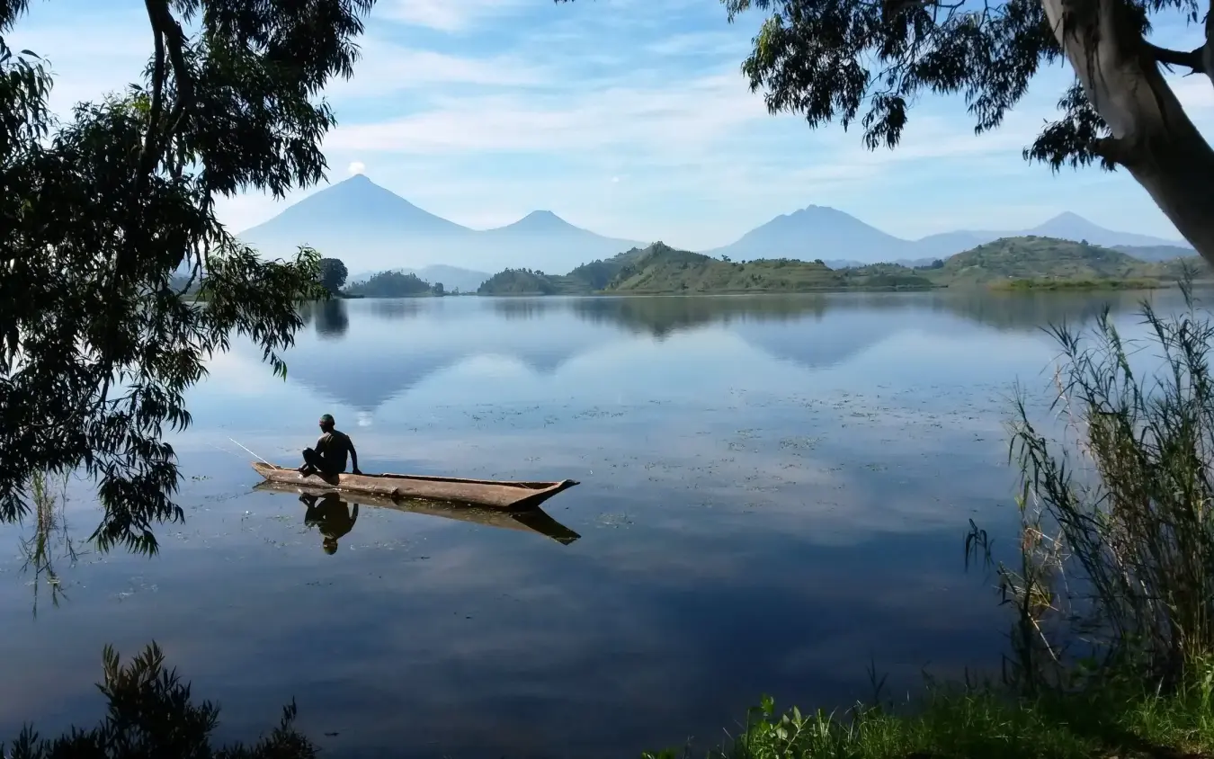 Fisherman in wooden boat on calm lake with volcanic peaks, Mutanda Lake Resort, Lake Mutanda, Uganda