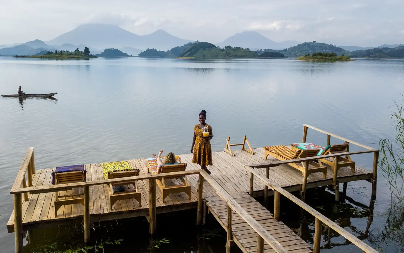 Person standing on wooden dock overlooking calm lake and mountains, Mutanda Lake Resort, Lake Mutanda, Uganda