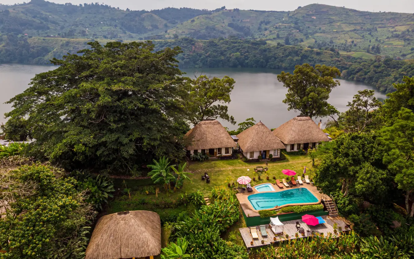 Thatched-roof lodge bungalows overlooking calm lake and hills, Ndali Lodge, Kibale Forest, Uganda