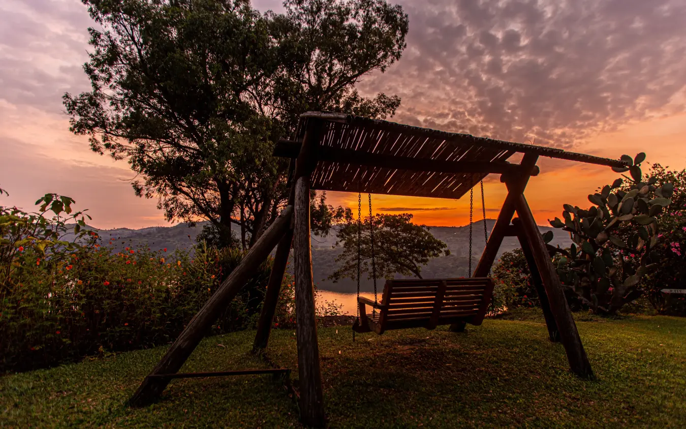 Wooden swing overlooking lake at sunset with mountains, Ndali Lodge, Kibale Forest, Uganda