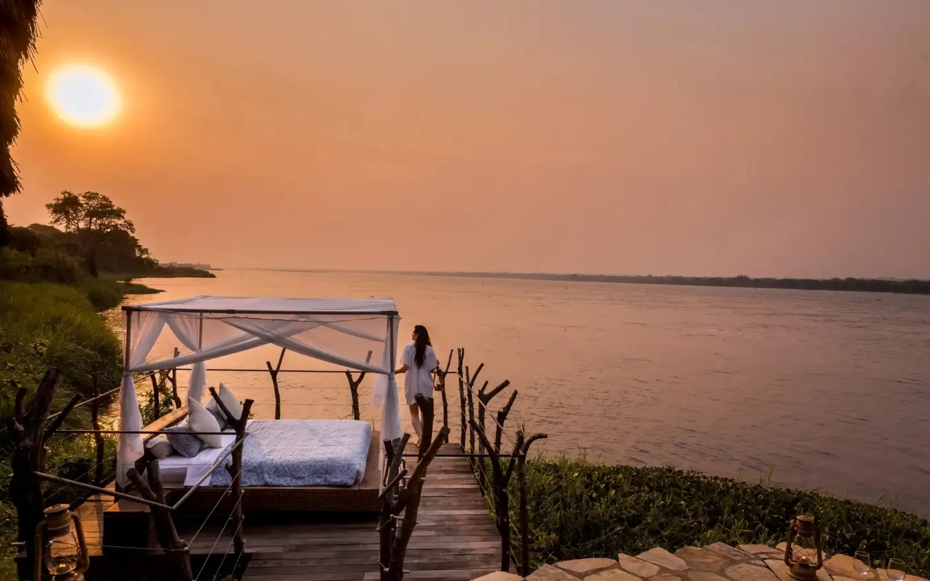 Waterfront deck with canopy bed overlooking river at sunset, Nile Safari Lodge, Murchison Falls NP, Uganda