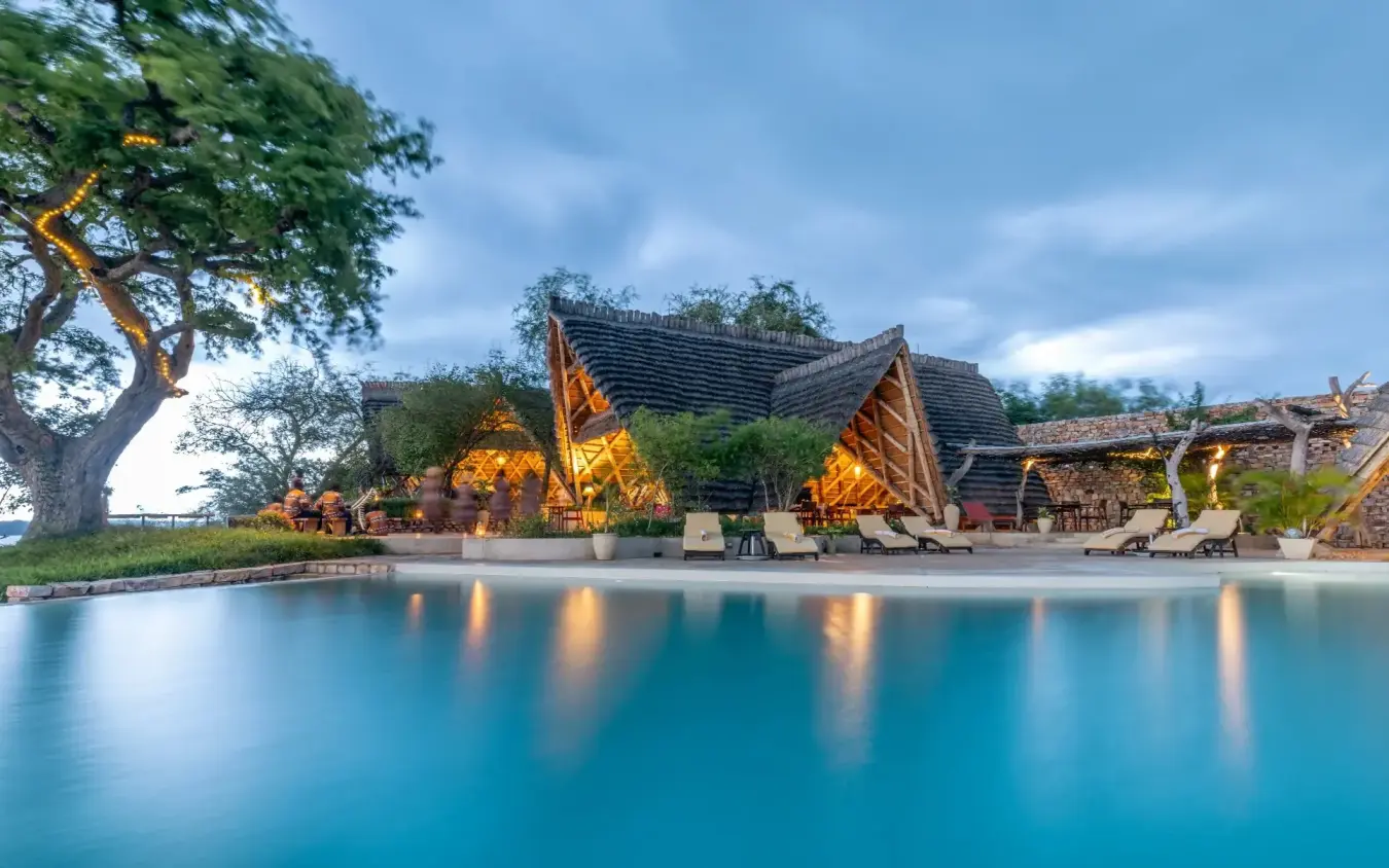 Illuminated lodge structures reflected in still water at dusk, Nile Safari Lodge, Murchison Falls NP, Uganda