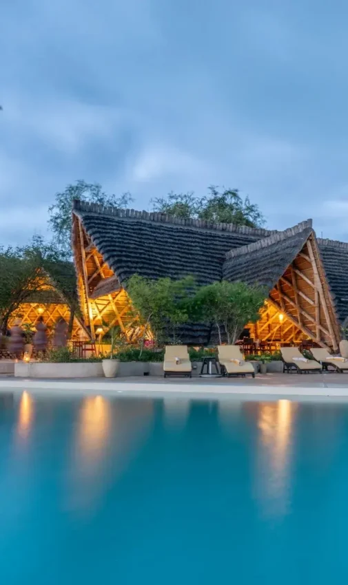 Illuminated lodge structures reflected in still water at dusk, Nile Safari Lodge, Murchison Falls NP, Uganda