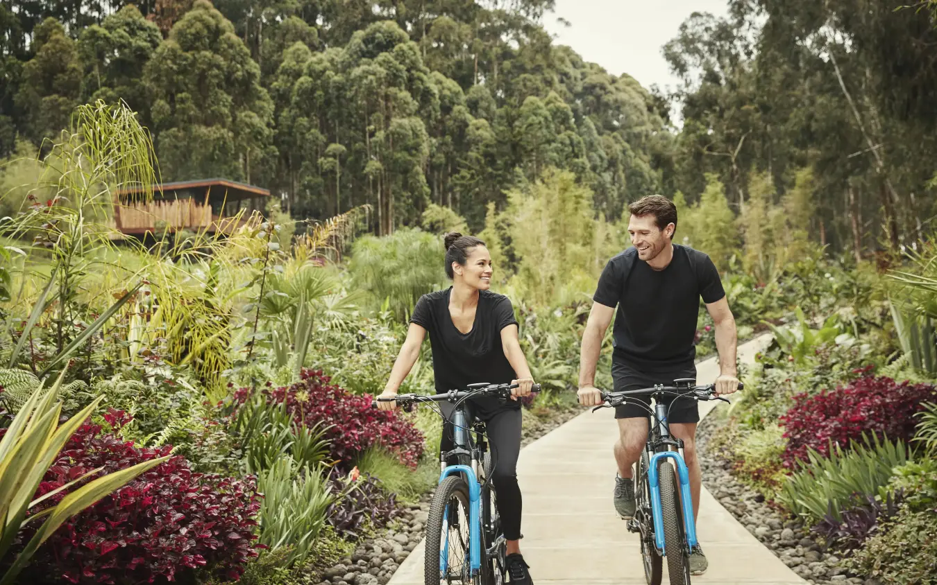 Two cyclists riding on wooden path through botanical gardens, Gorilla’s Nest, Volcanoes National Park, Rwanda