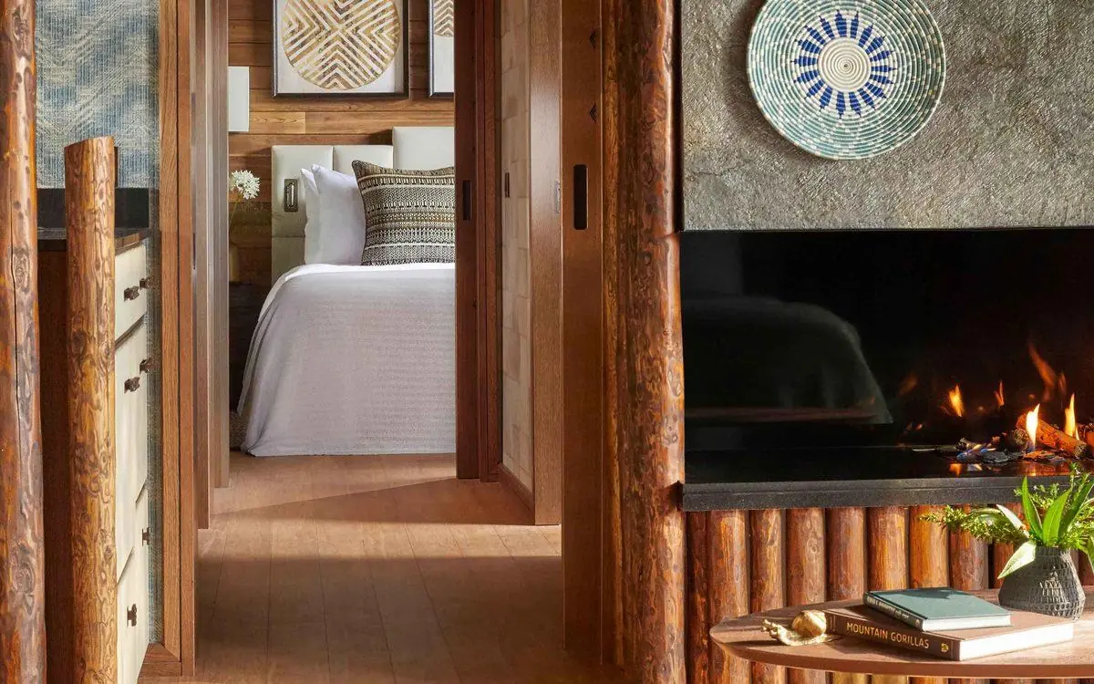 Bedroom with fireplace, wooden beams, and decorative wall art, Gorilla’s Nest, Volcanoes National Park, Rwanda