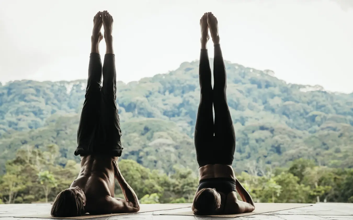 Two people practicing yoga headstand pose outdoors overlooking forested mountains, Nyungwe House, Nyungwe Forest, Rwanda
