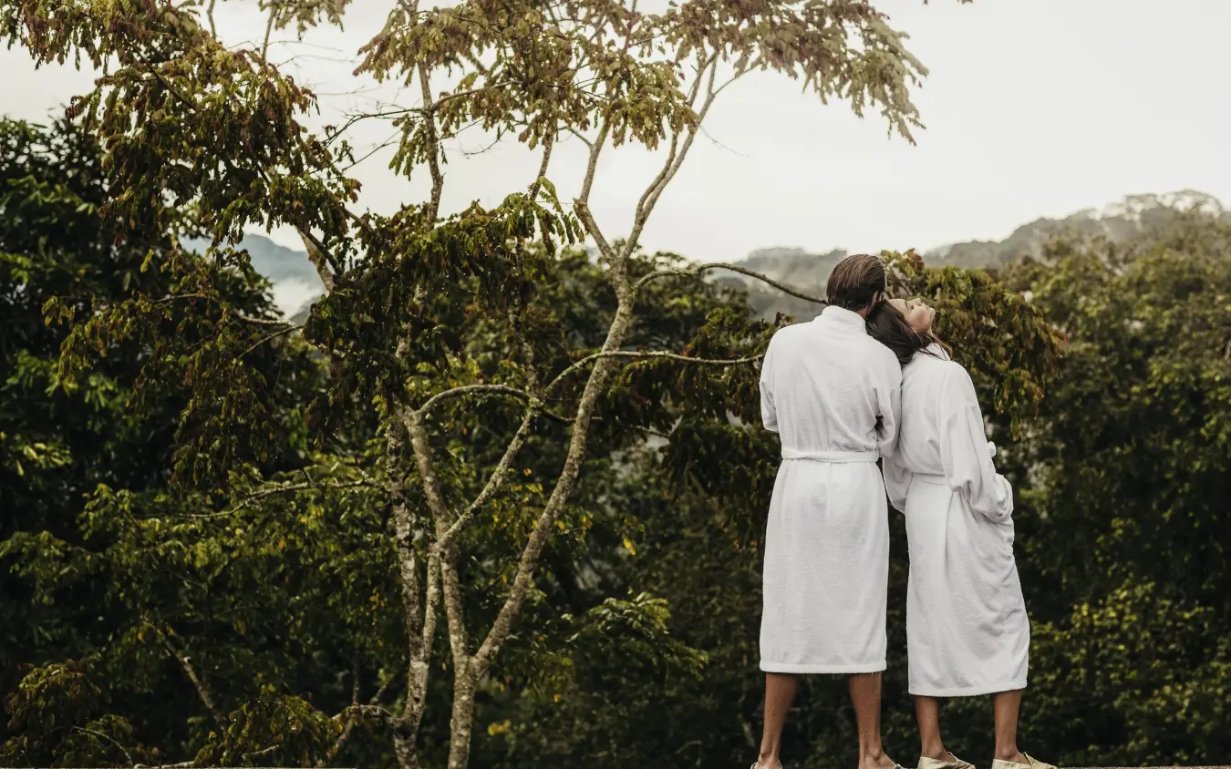 Two guests in white robes viewing forested landscape from deck, Nyungwe House, Nyungwe Forest, Rwanda
