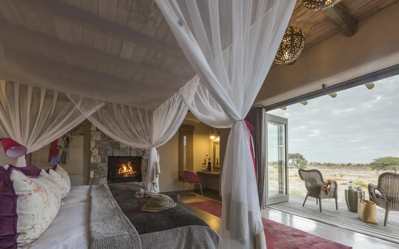 Bedroom with canopy bed, fireplace, and savanna view, Onguma The Fort, Etosha National Park, Namibia