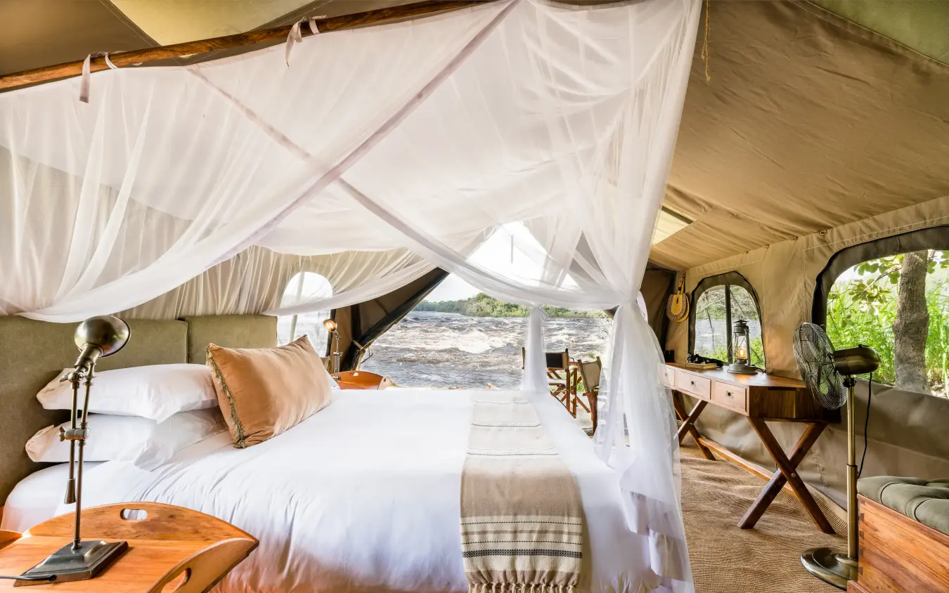Safari tent bedroom with draped canopy and wooden furniture, Papa’s Camp, Murchison Falls NP, Uganda