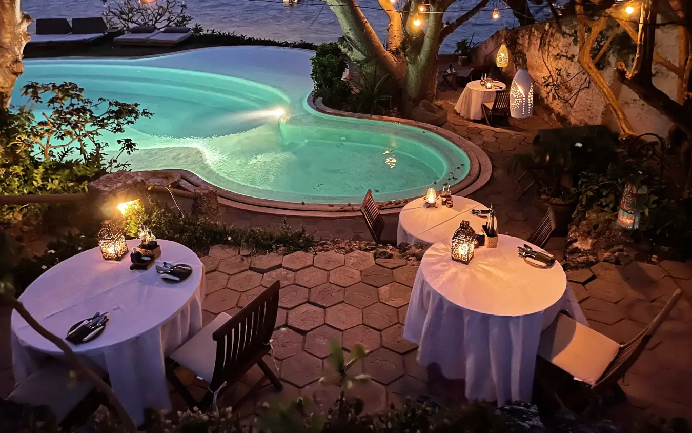 Illuminated curved swimming pool at dusk with dining tables, Peponi Hotel, Lamu Archipelago, Kenya