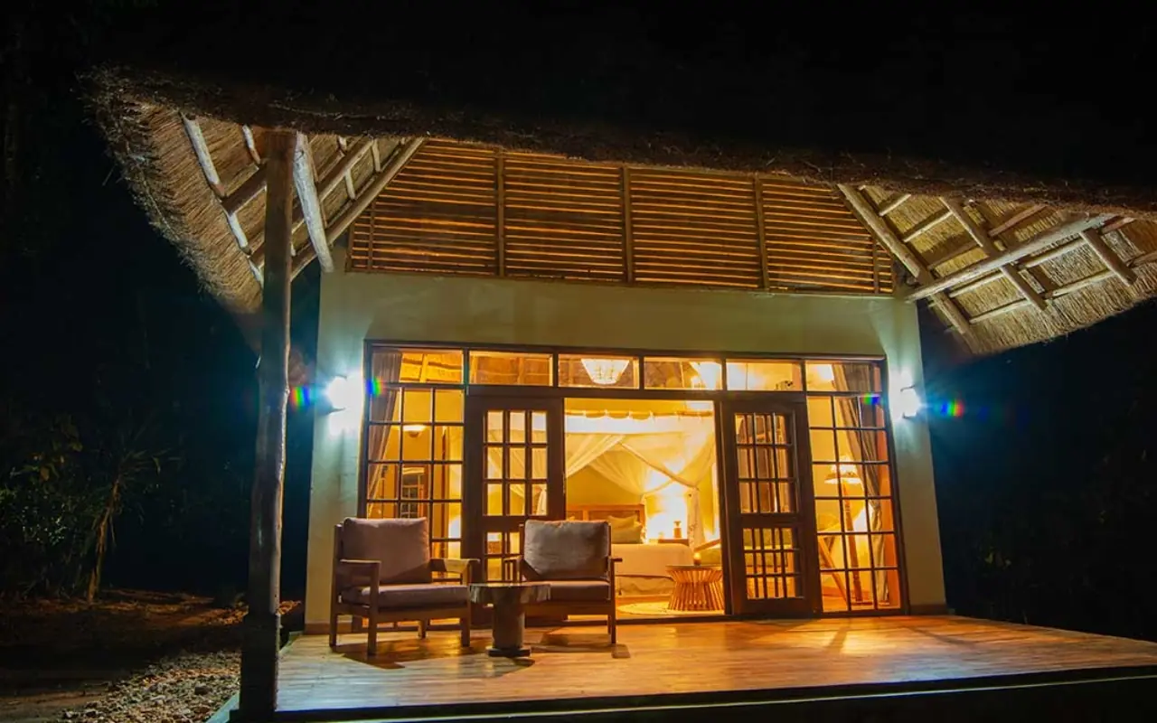 Illuminated lodge pavilion with wooden deck at night, Primate Lodge, Kibale Forest, Uganda