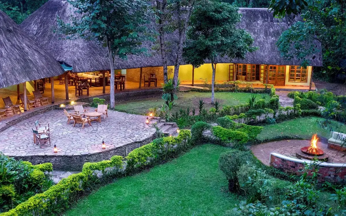 Illuminated lodge buildings with fire pit and manicured grounds at dusk, Primate Lodge, Kibale Forest, Uganda