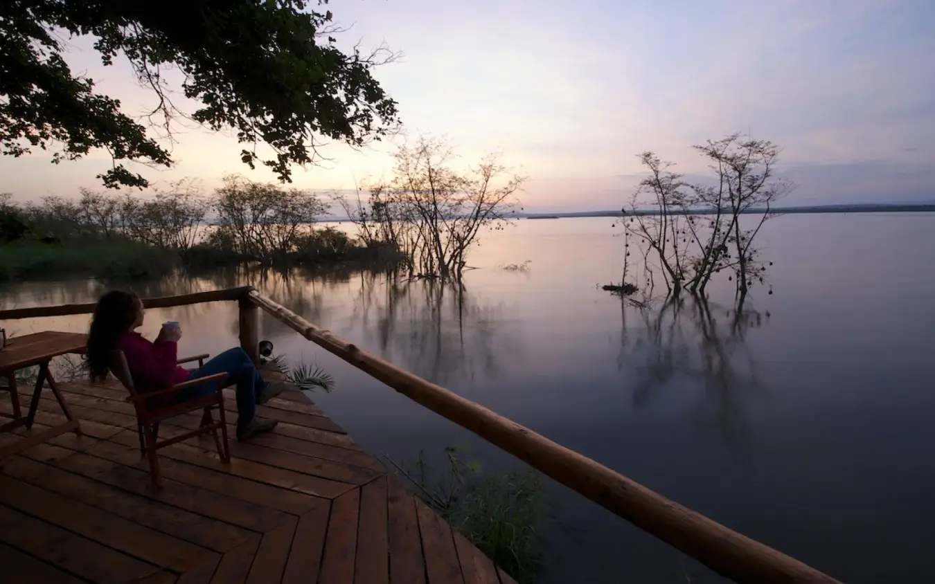 Guest relaxing on wooden deck overlooking calm water at dusk, Ruzizi Tented Lodge, Akagera National Park, Rwanda