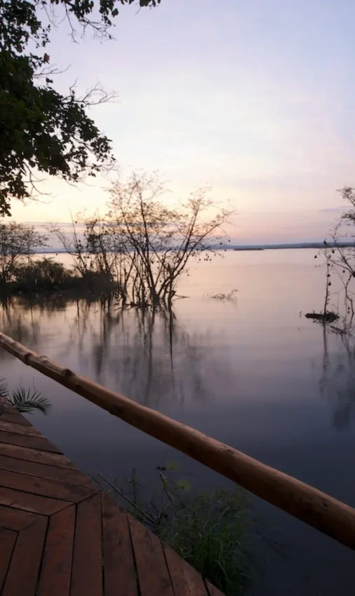 Guest relaxing on wooden deck overlooking calm water at dusk, Ruzizi Tented Lodge, Akagera National Park, Rwanda