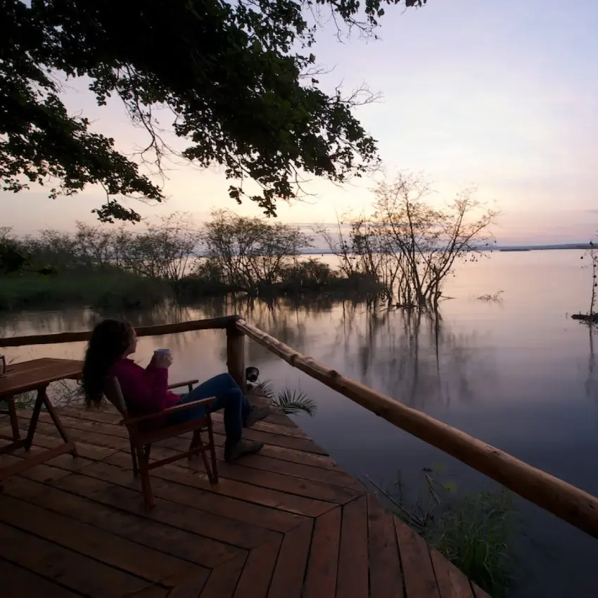 Guest relaxing on wooden deck overlooking calm water at dusk, Ruzizi Tented Lodge, Akagera National Park, Rwanda