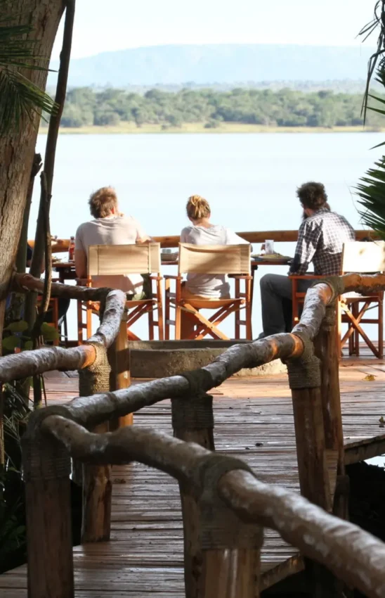 Guests relax on wooden deck overlooking river and forest, Ruzizi Tented Lodge, Akagera National Park, Rwanda