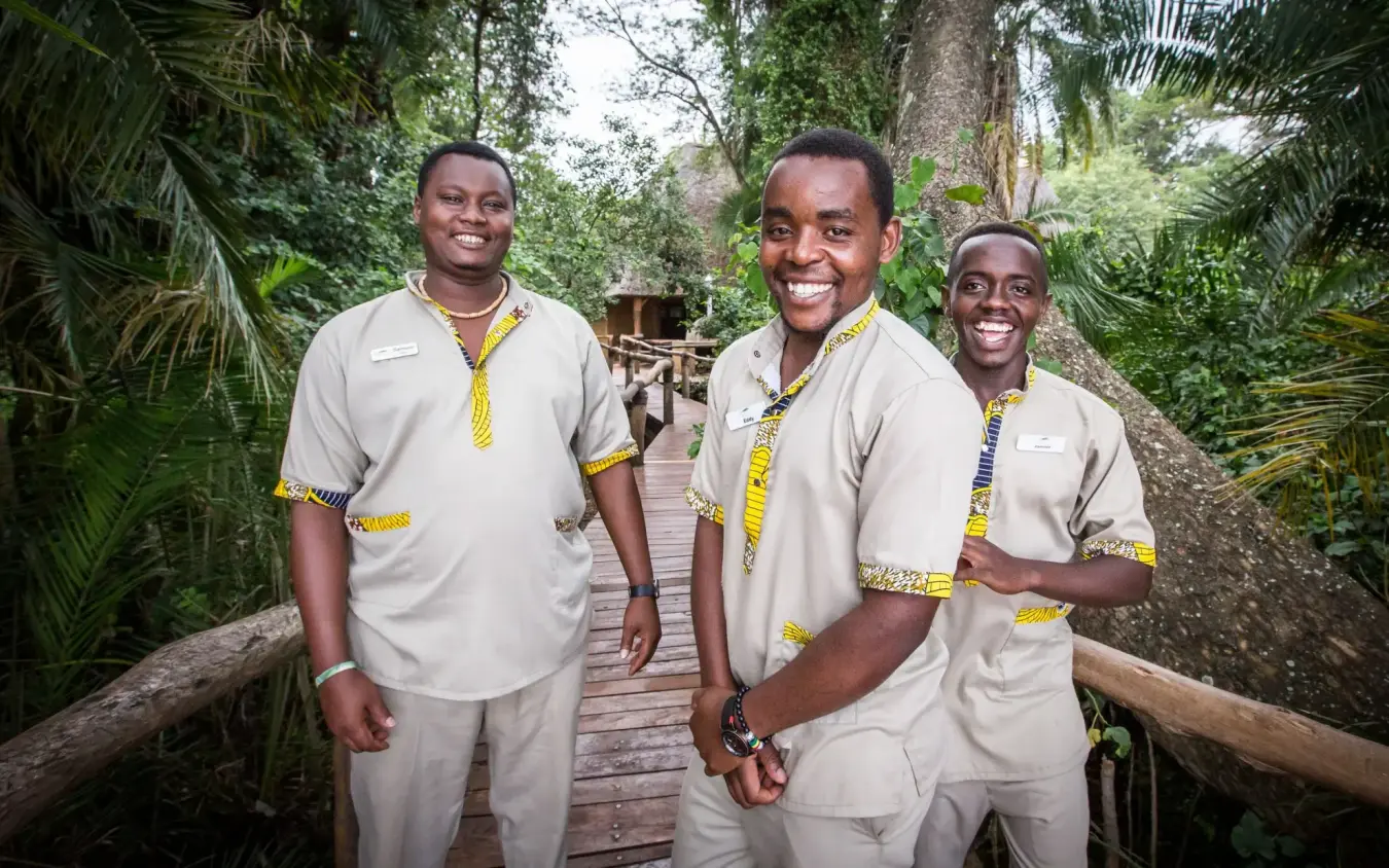 Three staff members smiling on wooden forest boardwalk, Ruzizi Tented Lodge, Akagera National Park, Rwanda