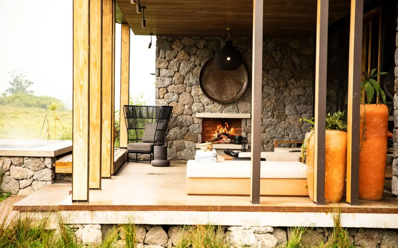Stone lodge deck with fireplace overlooking landscape, Singita Kwitonda Lodge, Volcanoes National Park, Rwanda