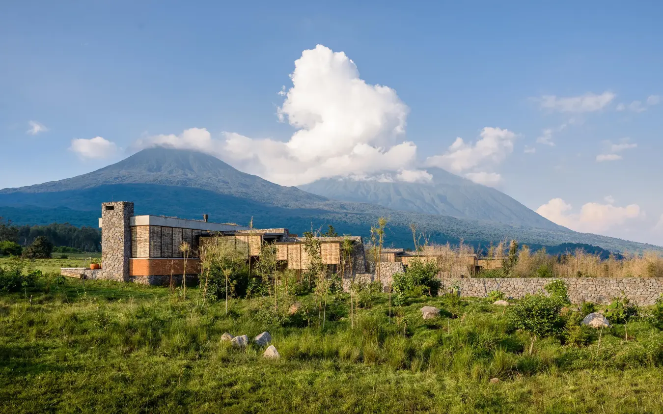 Modern lodge building with volcanic mountain backdrop and green fields, Singita Kwitonda Lodge, Volcanoes National Park, Rwanda