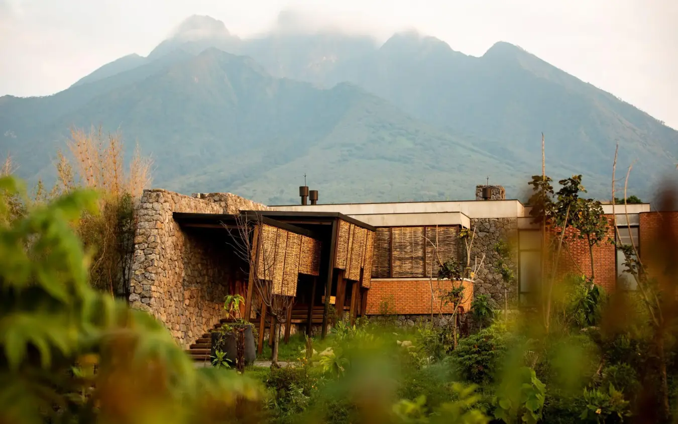 Modern brick lodge building with mountain backdrop and vegetation, Singita Kwitonda Lodge, Volcanoes National Park, Rwanda