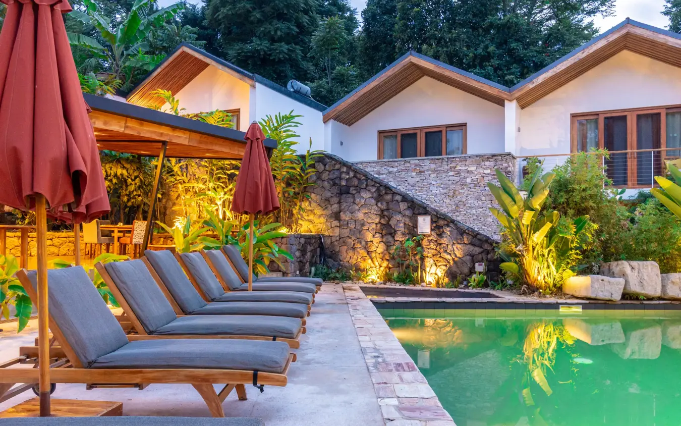 Loungers by illuminated pool with modern lodge buildings, Hemingways Retreat Kigali, Kigali, Rwanda