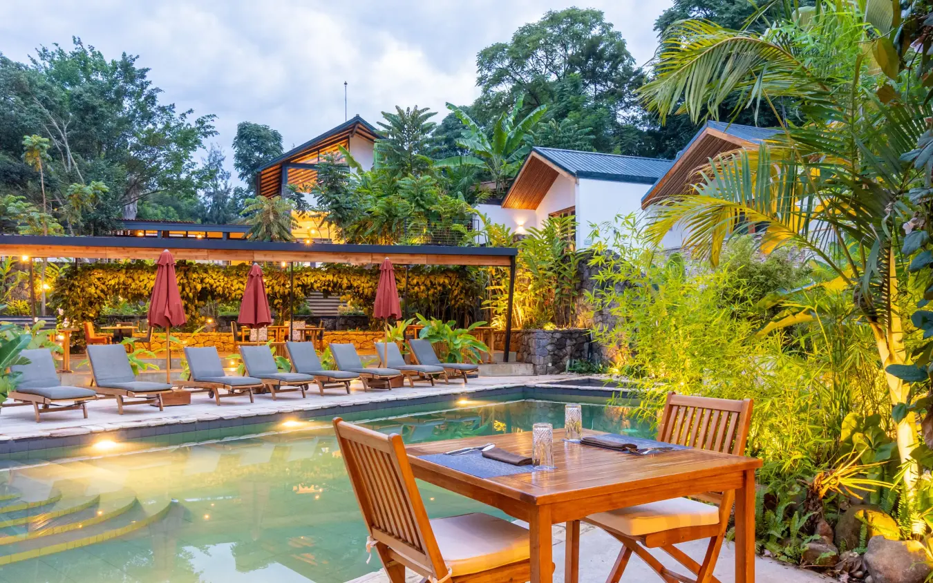 Illuminated pool area with lounge chairs and dining table at dusk, Hemingways Retreat Kigali, Kigali, Rwanda