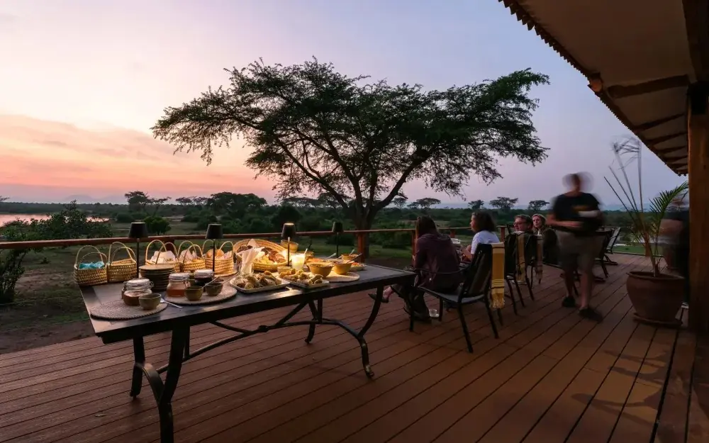 Sunset dining setup on wooden deck overlooking river landscape, The River Station, Queen Elizabeth NP, Uganda