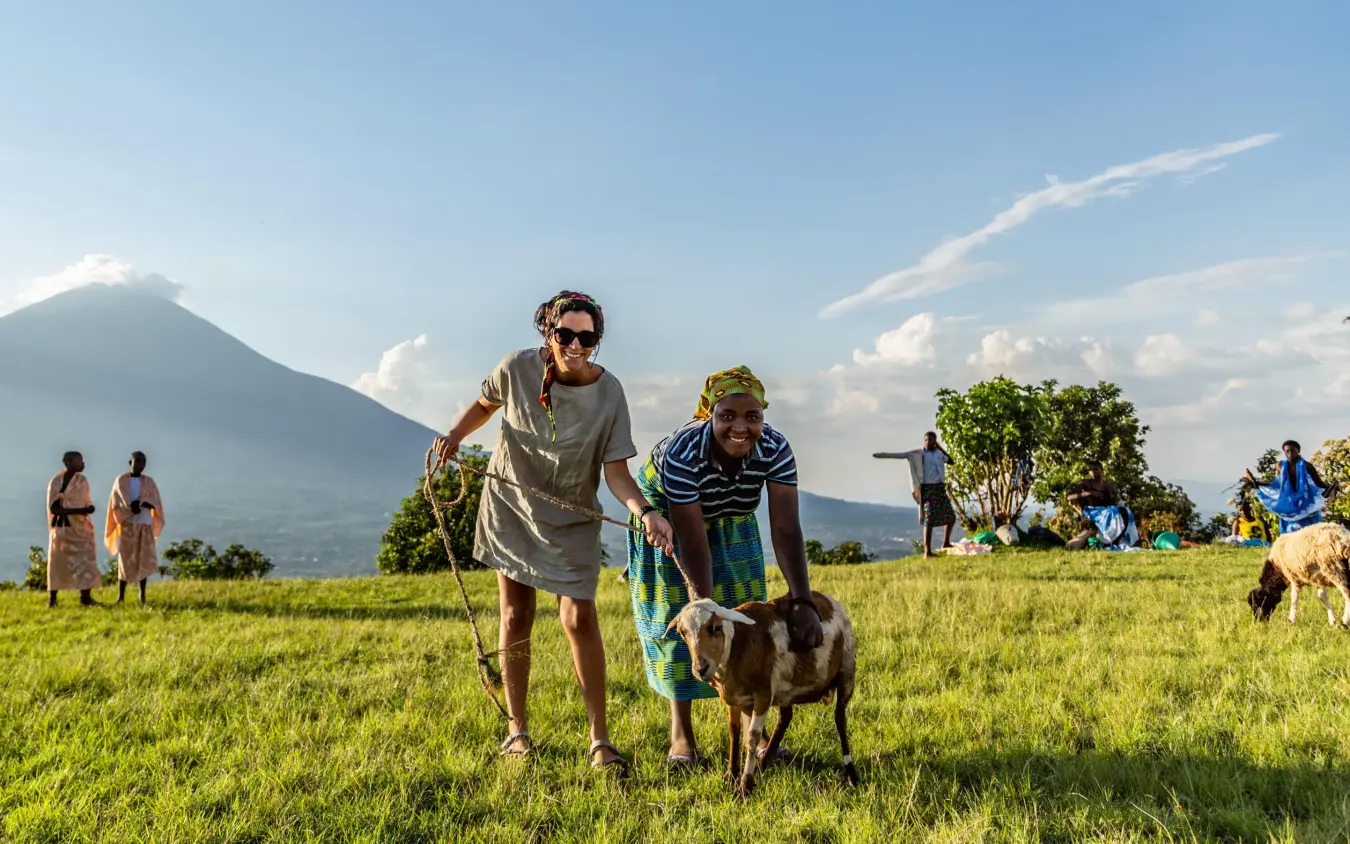 Guests walking with goats in green valley landscape, Virunga Lodge, Volcanoes National Park, Rwanda