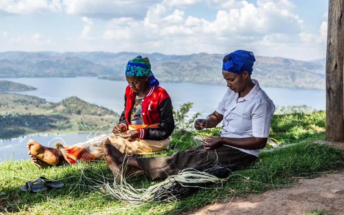 Two people crafting traditional baskets overlooking a lake valley, Virunga Lodge, Volcanoes National Park, Rwanda