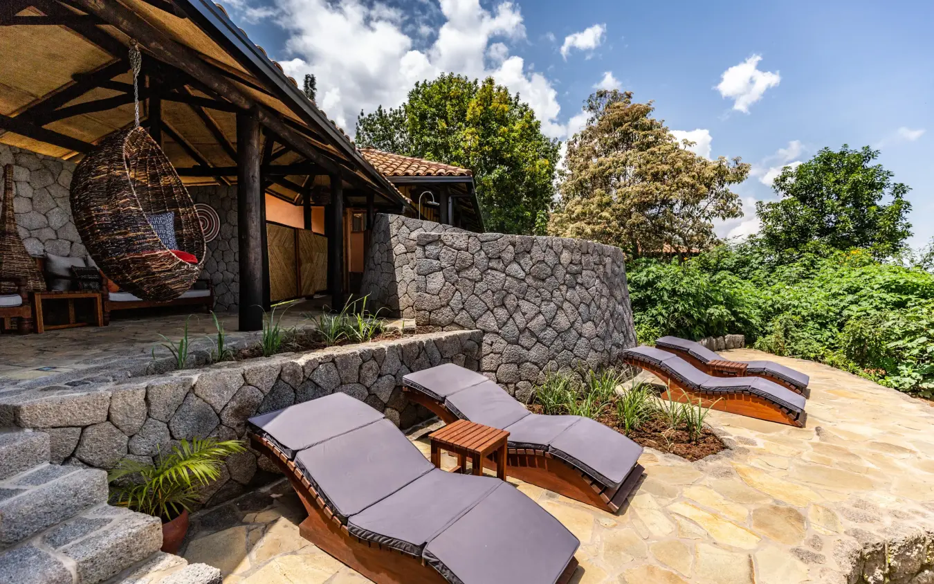 Stone terrace with lounge chairs overlooking forested landscape, Virunga Lodge, Volcanoes National Park, Rwanda