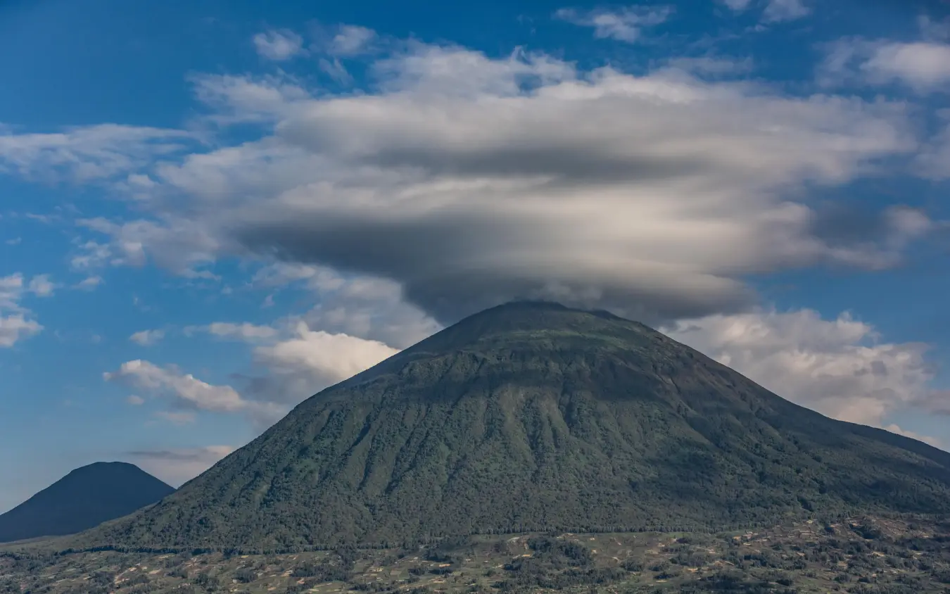 Symmetrical volcanic cone mountain under cloudy blue sky, Virunga Lodge, Volcanoes National Park, Rwanda
