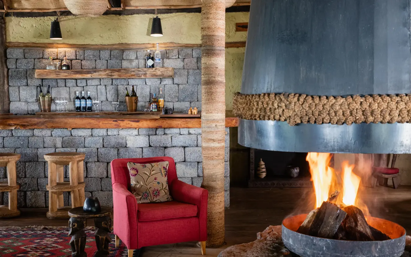 Stone fireplace lounge with red armchair and central fire pit, Virunga Lodge, Volcanoes National Park, Rwanda