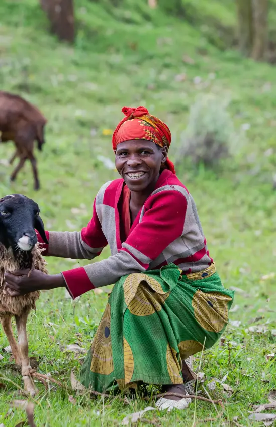Local herder smiling with goat in grassy hillside, Virunga Lodge, Volcanoes National Park, Rwanda