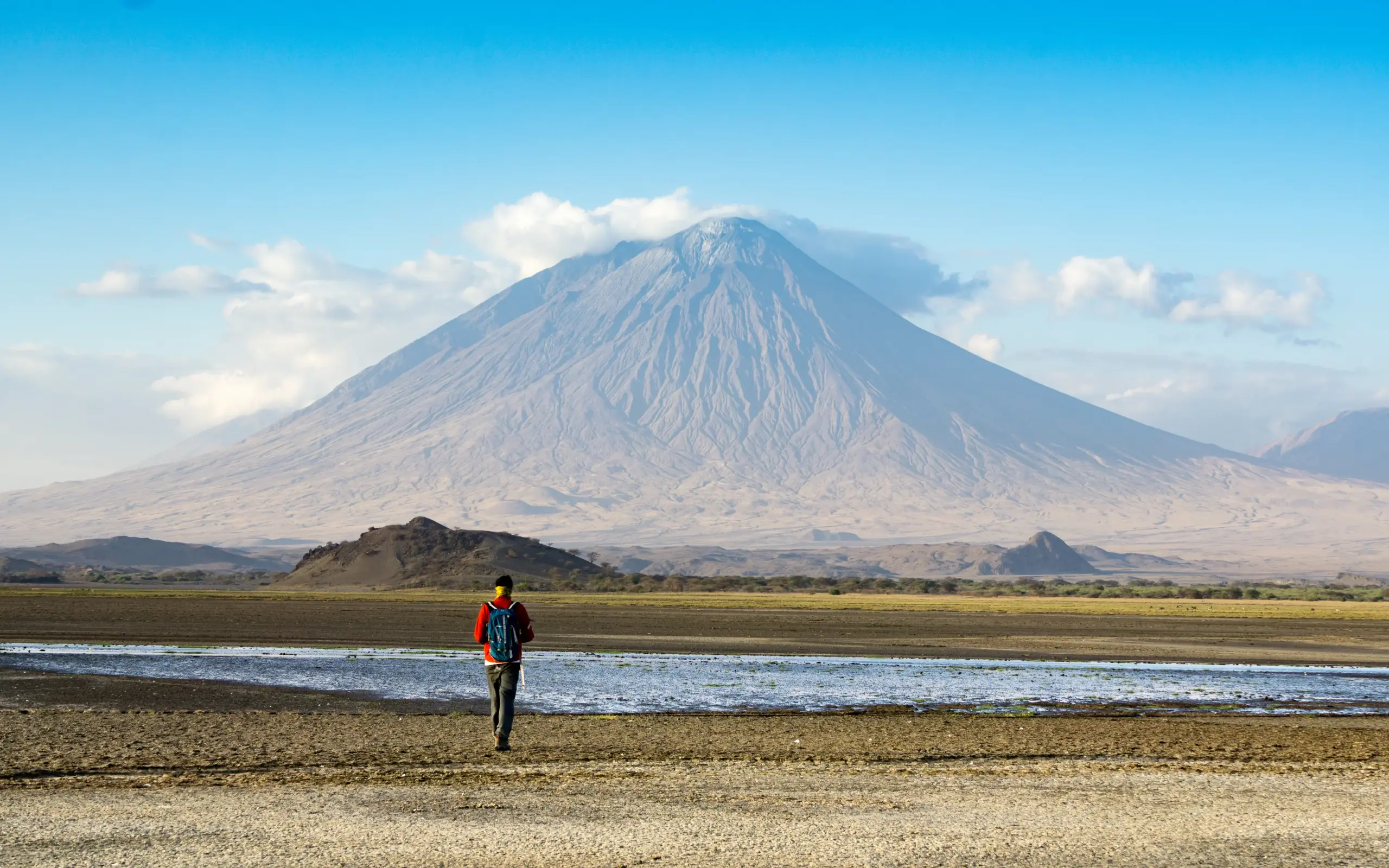 Hiker in orange jacket running toward volcanic mountain
