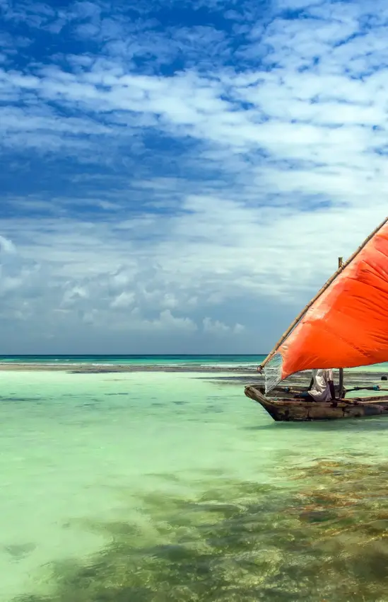 Traditional sailing dhow with red sail in shallow turquoise water