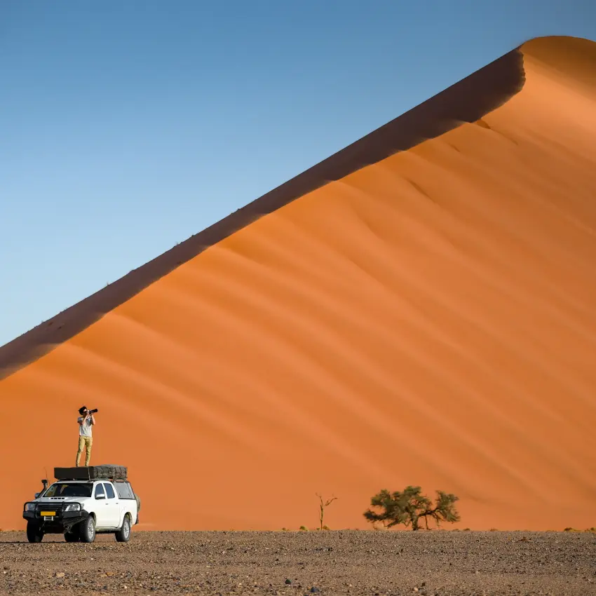 Person standing on vehicle roof overlooking massive sand dune