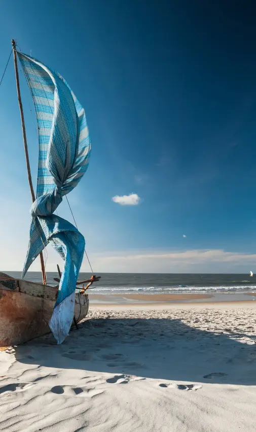 Traditional fishing boat with blue sail on sandy beach
