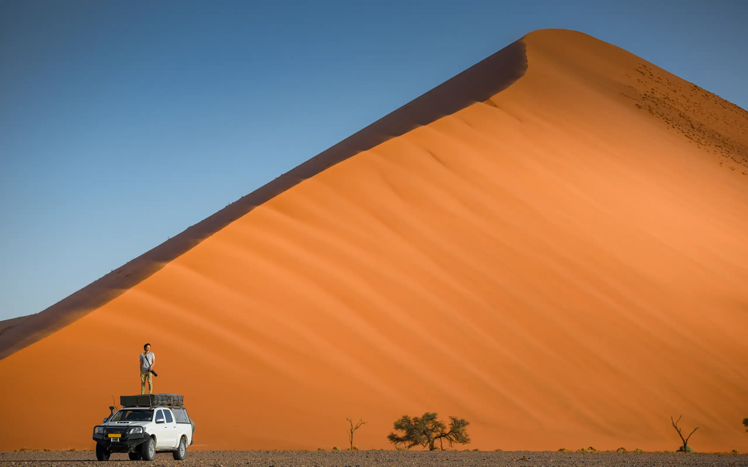 Person standing on vehicle before massive sand dune