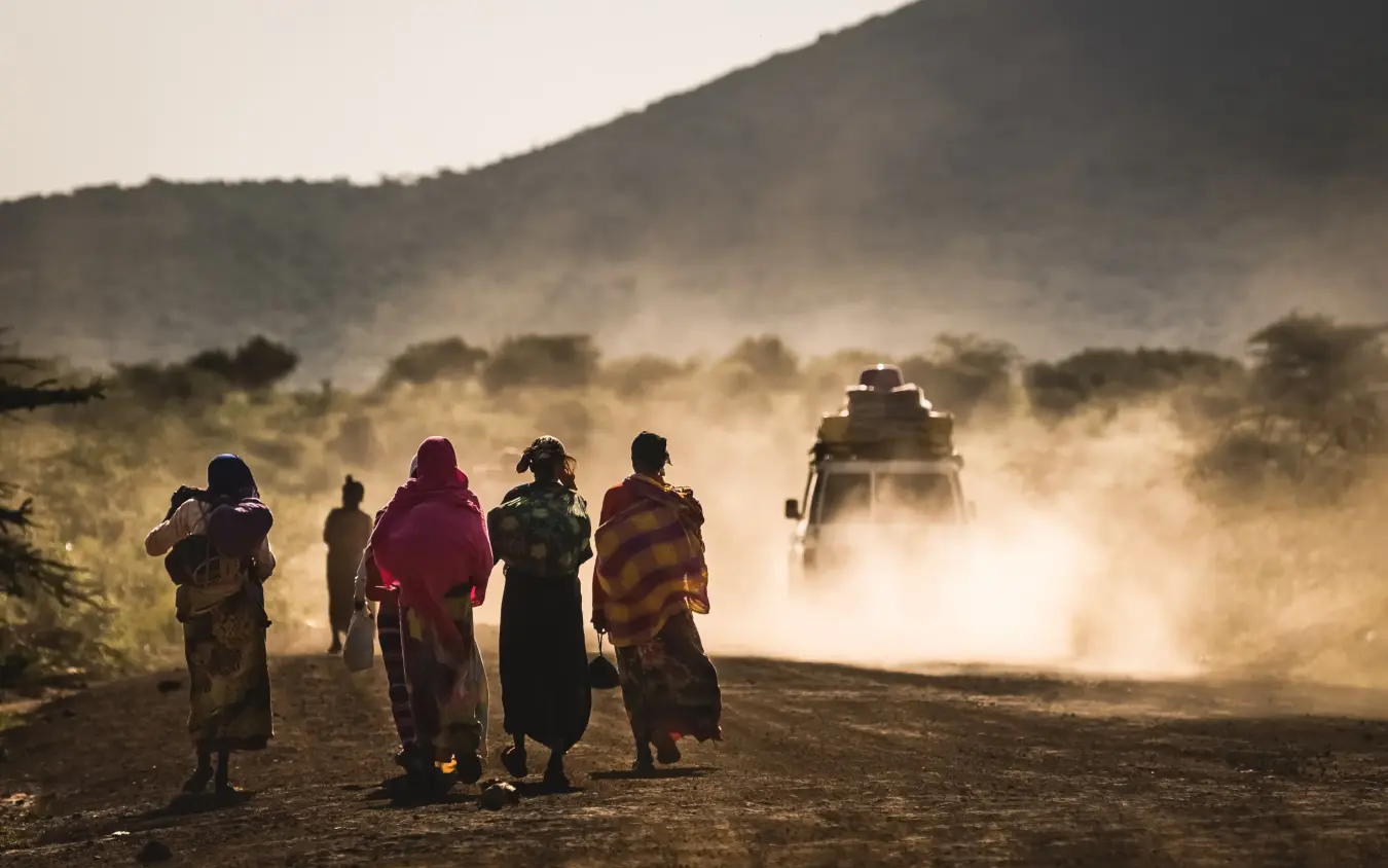 Local people walking on dusty road with vehicle approaching