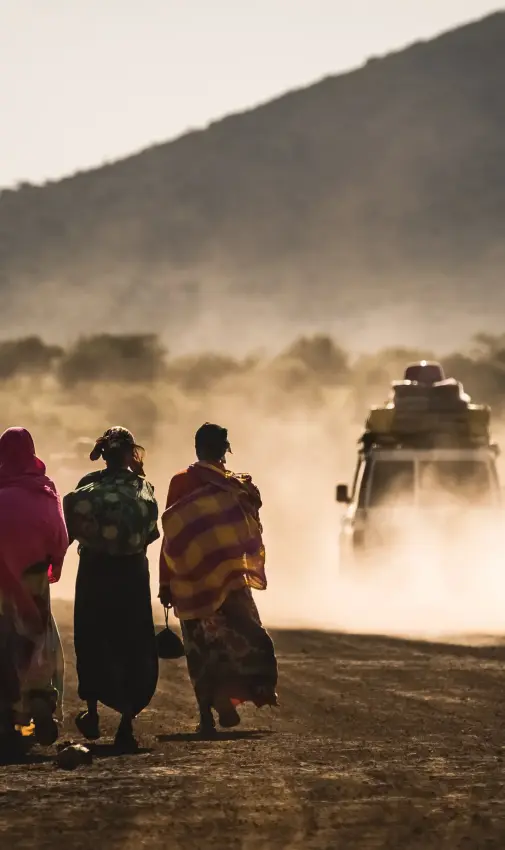 Local people walking on dusty road with vehicle approaching