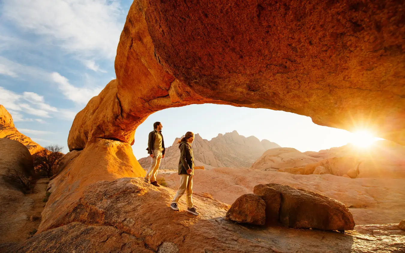 Hikers explore natural rock arch at sunset in desert